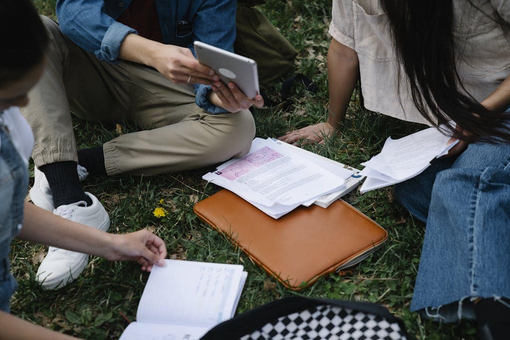 Best online writing groups - A group of students studying together outside, using a tablet and papers on the grass.