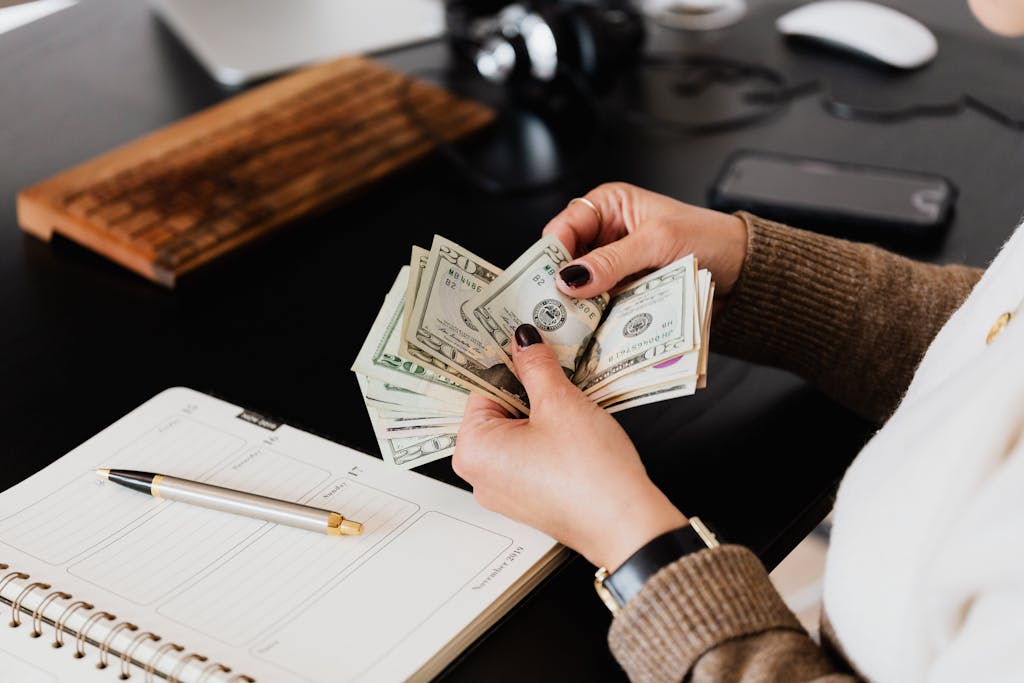 Make money from writing: Female in sweater counting dollar bills while sitting at wooden table with planner and pen